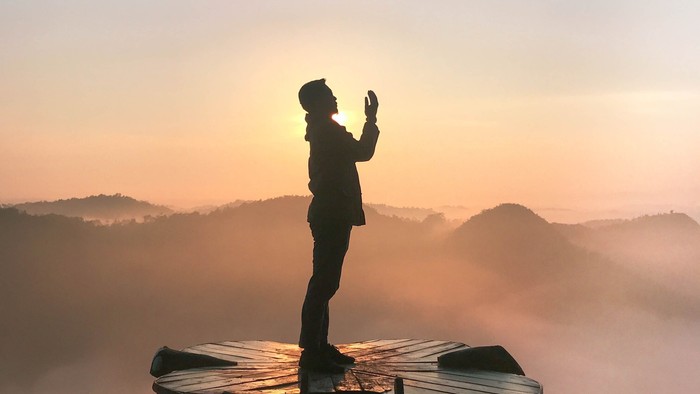 Person steht auf einem Tisch und fotografiert Sonnenaufgang