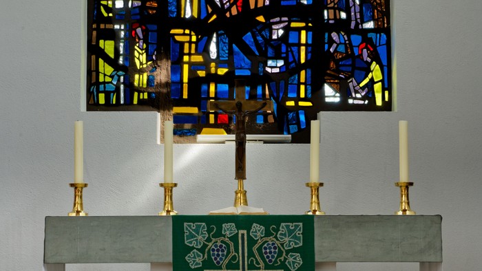 Farbenfrohes Kirchenfenster über einem Altar mit Kerzen und grünem Tuch