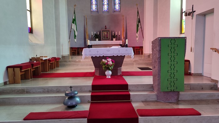 Eleganter Kircheninnenraum mit Altar, geschmückt mit Blumen, roten Teppichstufen und grünen Beichtstühlen.