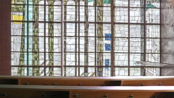 Buntes Kirchenfenster mit Holzrahmen und Sitzbank davor