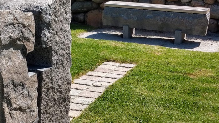 En grøn plæne med en granitbank og en mur af natursten.