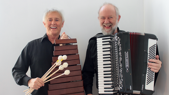 To glade mænd holder en marimba og en harmonika, og smiler til kameraet.