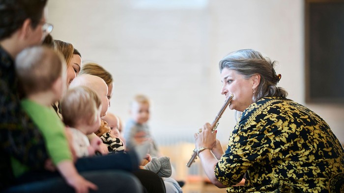 En kvinde i mønstrede jakke taler i et mikrofon til en forsamling.