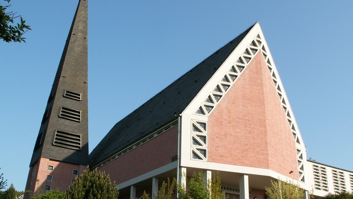 Moderne Kirche mit hohem Turm und geometrischem, dreieckigem Architekturdesign vor klarem Himmel.
