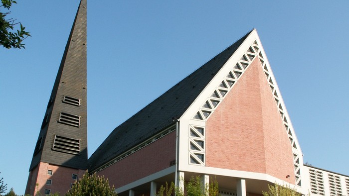 Moderne Kirche mit hohem Turm und geometrischem, dreieckigem Architekturdesign vor klarem Himmel.