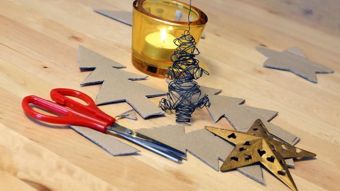 Auf dem Holztisch liegen eine brennende Kerze, eine Schere, eine Drahtfigur und eine goldene Sterndekoration.