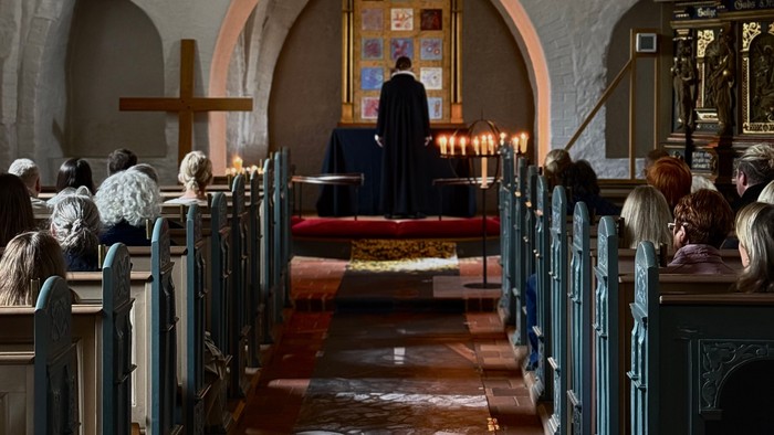 En præst står ved alteret i en kirke, omgivet af en forsamling.