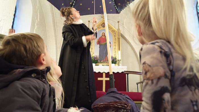 En præst velsigner et barn under en blå paraply med stjerner.