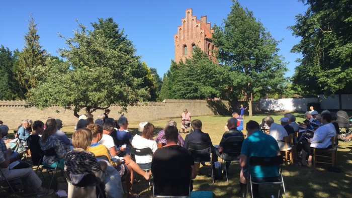 En gruppe af mennesker sidder på stolene i en park med et tårn i baggrunden