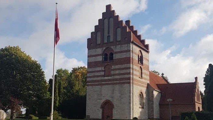 En kvinde går forbi en historisk bygning med tårn og flagstang.
