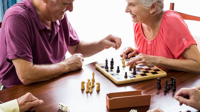 Ein älteres Paar spielt Schach an einem Tisch mit anderen Senioren.