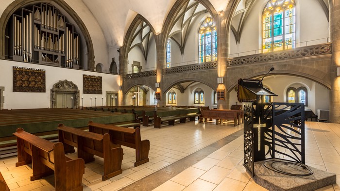 Innenraum einer Kirche mit Bänken, Orgel und bunten Fenstern
