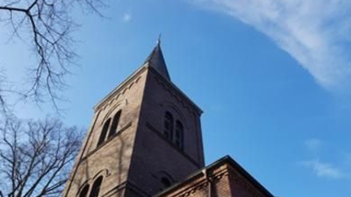 Ein hoher Kirchturm ragt vor einem klaren blauen Himmel auf.