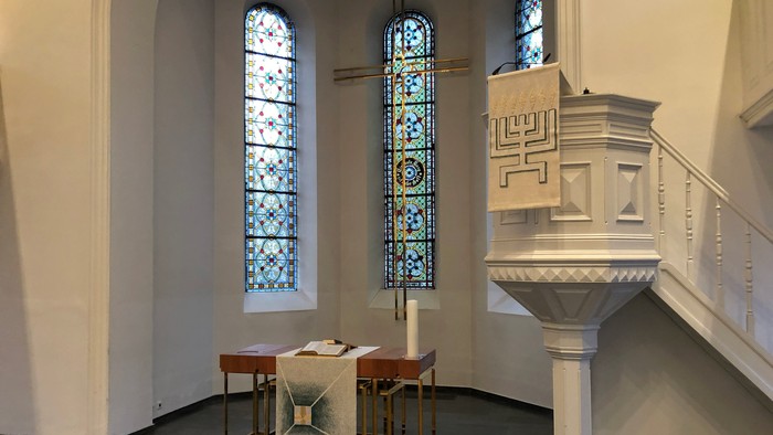 Historisches Synagogeninneres mit einem hölzernen Toraschrein, einer Kanzel und farbenfrohen Buntglasfenstern.