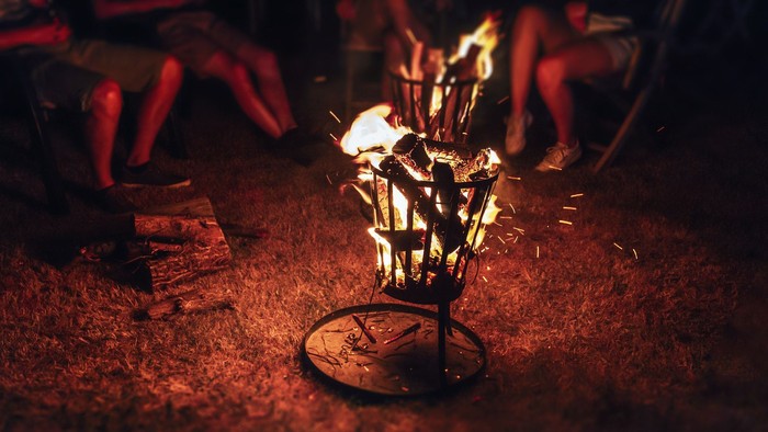 Im Schein des Feuers sitzt eine Gestalt auf einem Stuhl, umgeben von Flammen.