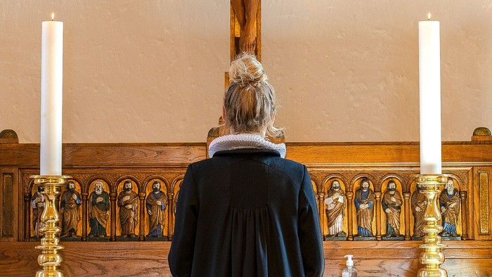 Kvinde i mørkt kapel med lysede steariner og alter.
