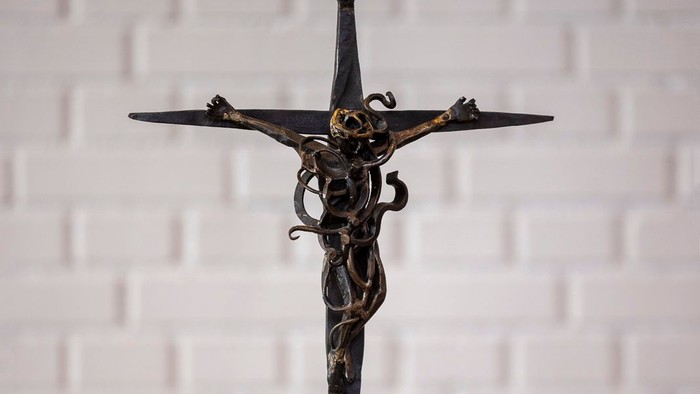 En smedejernskulptur af Jesus Kristus på korset står på en hvid flise.