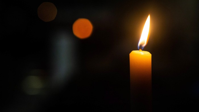 A single lit candle in darkness with blurred lights.