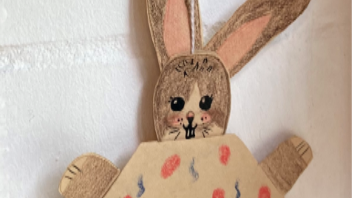 Ein selbstgemachtes Osterhasen-Dekoration aus Pappe mit Kleid und bunten Eiern.