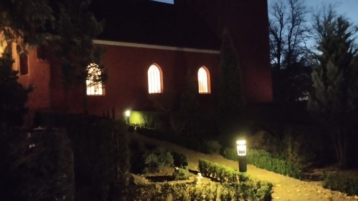 En mørk nattehavende kirke med lysende vinduer og belysning i have.