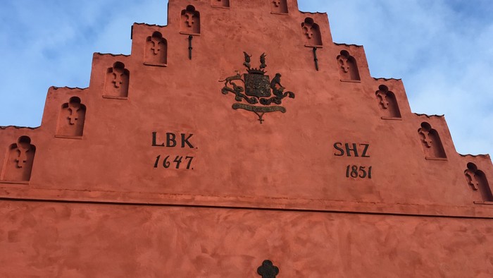Bygningen har en rosafarget farve og en pyramideformet gavl med skærgårdsmotiver og datering.