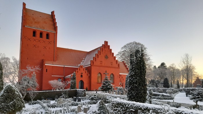 Rødt kirke med snødekt have og træer