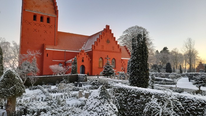 Rødt kirke med snødekt have og træer