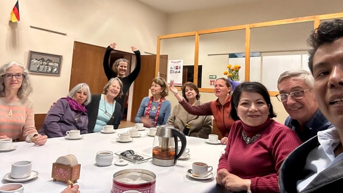 Eine Gruppe von Menschen sitzt an einem Tisch mit Kaffee und Kuchen und lacht.