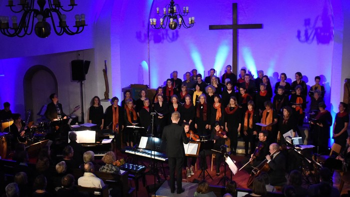 Eine große Gruppe von Musikern und Sängerinnen tritt in einer Kirche auf, begleitet von einem Orchester.
