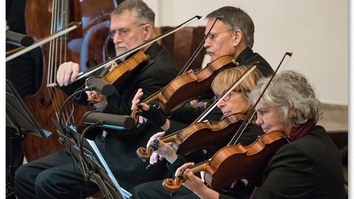 Eine Gruppe von Musiker:innen, die in einem Konzert Streichinstrumente spielen und sich konzentriert auf ihren Auftritt fokussieren.