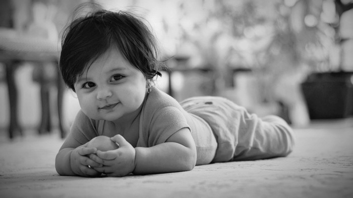 Nysgerrig småbarn liggende på gulvet med et blidt, tilfreds smil udendørs.