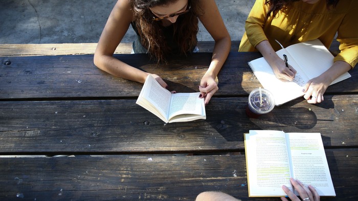 Zwei Frauen sitzen auf einer Holzbank und lesen Bücher.