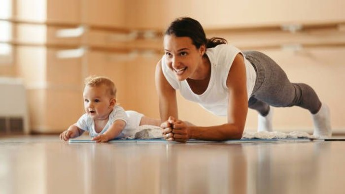 Eine Frau macht Yoga neben ihrem Baby auf einer Matte.