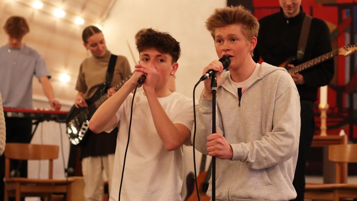 To young dren synger i mikrofoner mens to andre spiller guitar