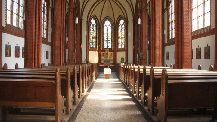 Innenraum einer Kirche mit Holzgestühl und hohen Fenstern
