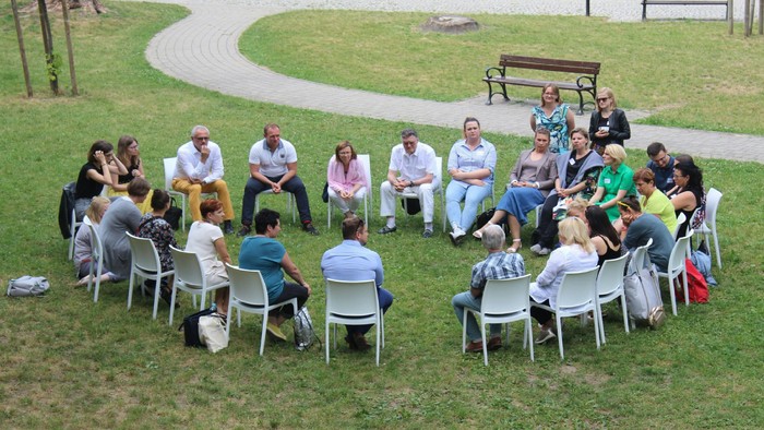Eine Gruppe von Menschen sitzt im Kreis auf Stühlen im Park und diskutiert.