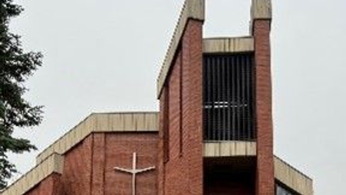 Das Bild zeigt eine moderne Ziegelkirche mit Kreuz und hohem Turm.