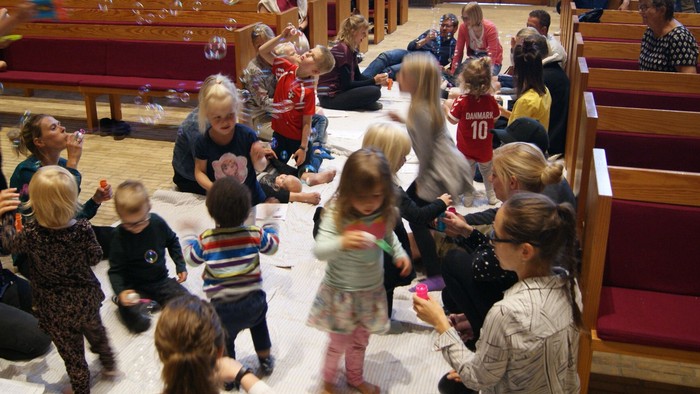Børn og voksne samles i kirke for aktivitet med boble.