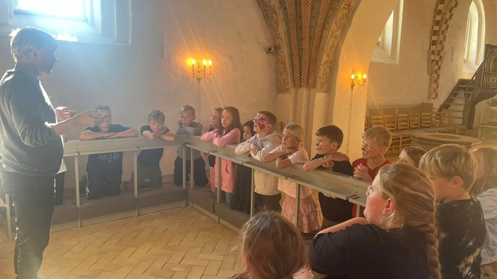 En gruppe børn og en voksne kvinde står i en historisk bygning og ser opad.