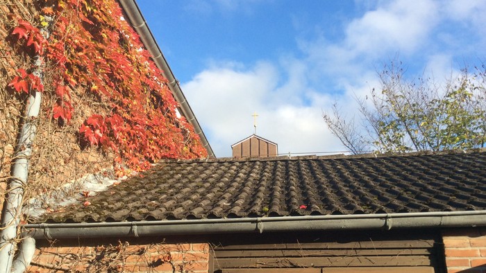 Das Bild zeigt ein altes Ziegelgebäude mit rotem Efeu und einem Schieferdach unter einem klaren blauen Himmel.