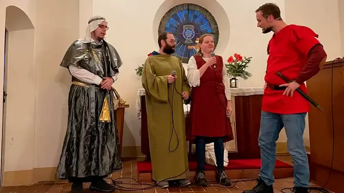 Vier Personen in historischen Kostümen stehen in einem Raum mit Kirchenfenster.