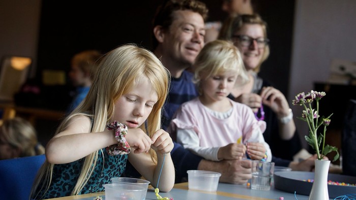 Børn og voksne sidder ved bord og laver håndarbejde