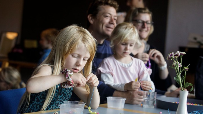 Børn og voksne sidder ved bord og laver håndarbejde