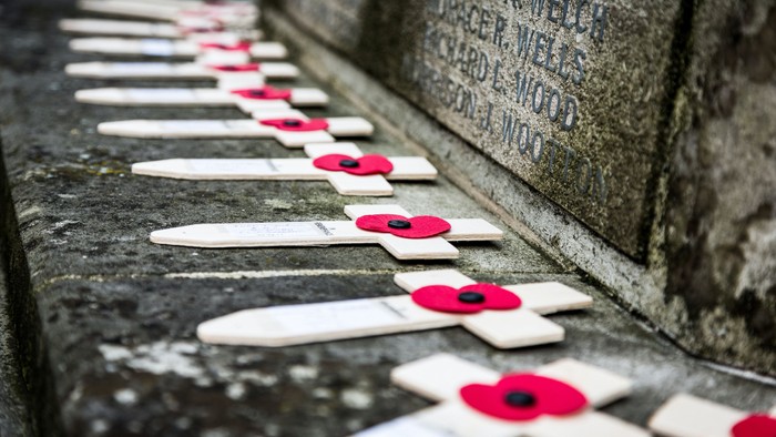Row of white crosses with red poppies on stone surface.