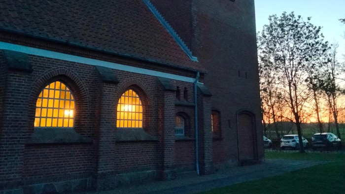 En murstenet kirke med spids tak og lysende vinduer ved solnedgang