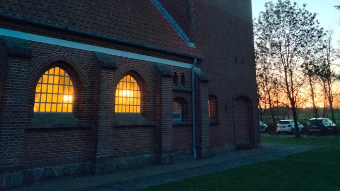 En murstenet kirke med spids tak og lysende vinduer ved solnedgang