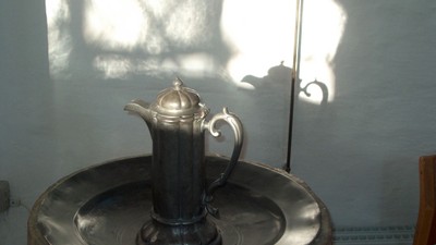 En sølv tekanne står på en metall underlag i sollys.