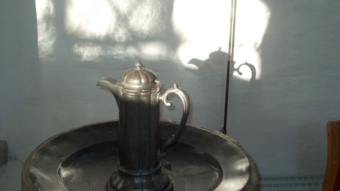En sølv tekanne står på en metall underlag i sollys.