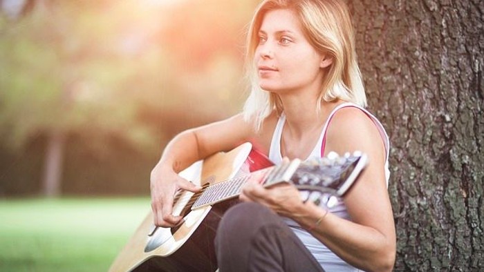 Junges Mädchen spielt Gitarre unter einem Baum