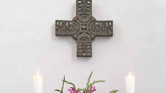 Ein Kreuz, zwei Kerzen, eine Vase mit Blumen und eine offene Bibel auf einem Tisch
